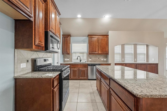 kitchen featuring light stone countertops, appliances with stainless steel finishes, a center island, and sink