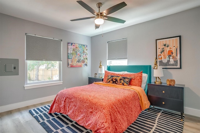 bedroom with ceiling fan, light hardwood / wood-style floors, electric panel, and multiple windows