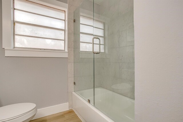 bathroom featuring hardwood / wood-style floors, toilet, and bath / shower combo with glass door