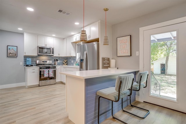 kitchen with kitchen peninsula, a breakfast bar, stainless steel appliances, pendant lighting, and white cabinets