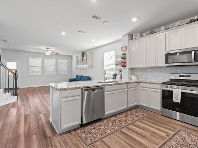 kitchen with stainless steel appliances, sink, white cabinetry, kitchen peninsula, and backsplash