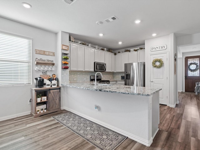 kitchen with kitchen peninsula, light stone countertops, backsplash, white cabinets, and appliances with stainless steel finishes