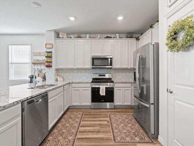 kitchen featuring stainless steel appliances, light stone countertops, sink, light hardwood / wood-style flooring, and white cabinetry