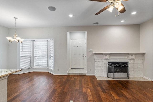 unfurnished living room featuring dark hardwood / wood-style floors, ceiling fan with notable chandelier, and a brick fireplace