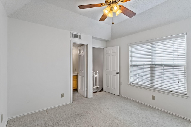 unfurnished bedroom with ensuite bath, ceiling fan, light colored carpet, a textured ceiling, and vaulted ceiling