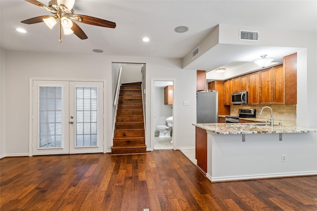 kitchen featuring appliances with stainless steel finishes, backsplash, light stone counters, kitchen peninsula, and french doors