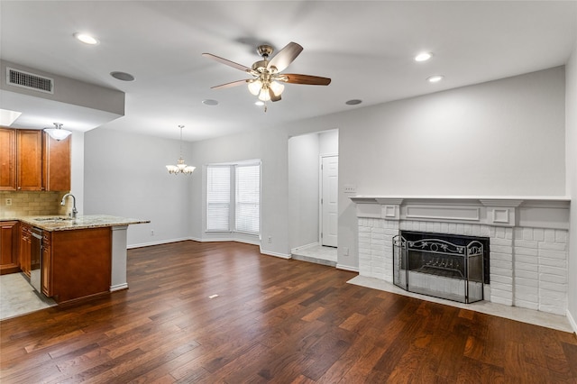 unfurnished living room featuring ceiling fan with notable chandelier, dark hardwood / wood-style floors, sink, and a brick fireplace