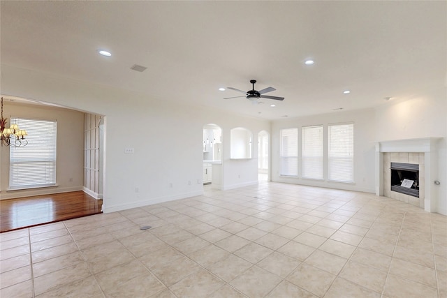 unfurnished living room featuring a healthy amount of sunlight, a fireplace, ceiling fan with notable chandelier, and light tile patterned floors