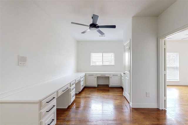 unfurnished office with dark hardwood / wood-style flooring, built in desk, and ceiling fan