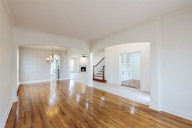 unfurnished living room with hardwood / wood-style flooring, ornamental molding, ceiling fan with notable chandelier, and built in shelves