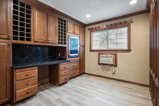 office space with a textured ceiling, light hardwood / wood-style floors, built in desk, and ornamental molding