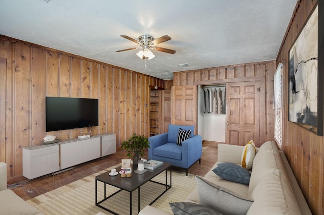 living room with ceiling fan, wood-type flooring, wooden walls, and a textured ceiling