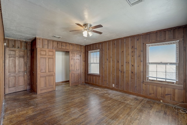 unfurnished bedroom with a textured ceiling, dark wood-type flooring, ceiling fan, and wood walls