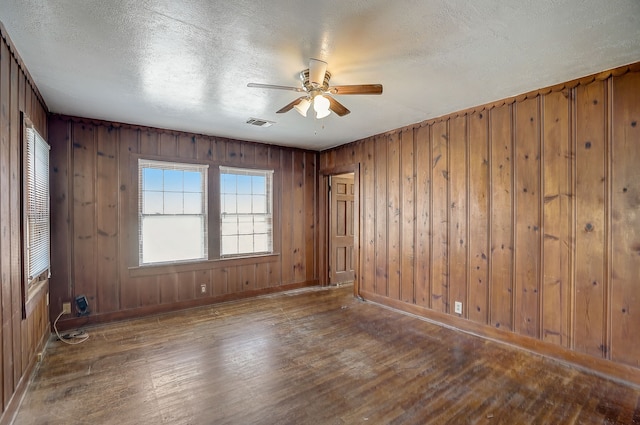 unfurnished room featuring wooden walls, ceiling fan, dark hardwood / wood-style flooring, and a textured ceiling