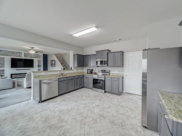 kitchen with gray cabinets, ceiling fan, appliances with stainless steel finishes, light stone counters, and kitchen peninsula