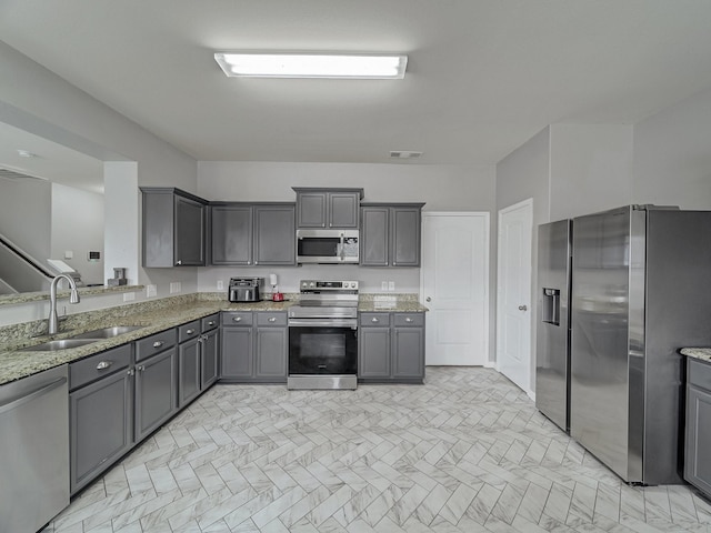 kitchen with light stone counters, appliances with stainless steel finishes, sink, and gray cabinetry