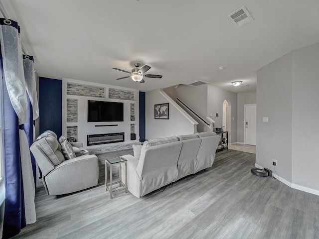 living room with built in shelves, a fireplace, light hardwood / wood-style floors, and ceiling fan