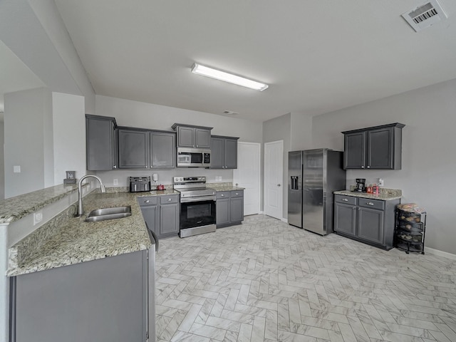 kitchen with gray cabinetry, sink, light stone counters, and appliances with stainless steel finishes