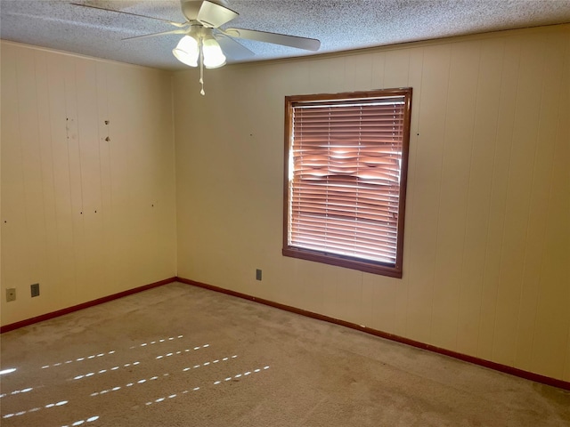 carpeted empty room with ceiling fan, wooden walls, and a textured ceiling