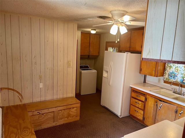 kitchen featuring wood walls, sink, ceiling fan, white fridge with ice dispenser, and washer / dryer