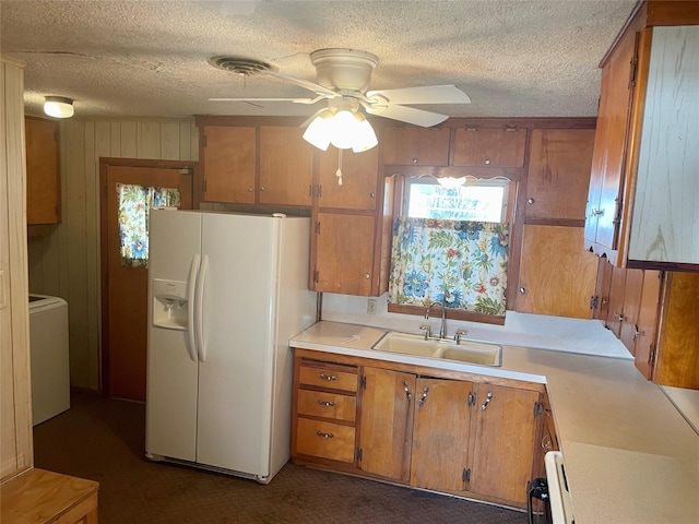 kitchen featuring ceiling fan, sink, white refrigerator with ice dispenser, washer / dryer, and wooden walls