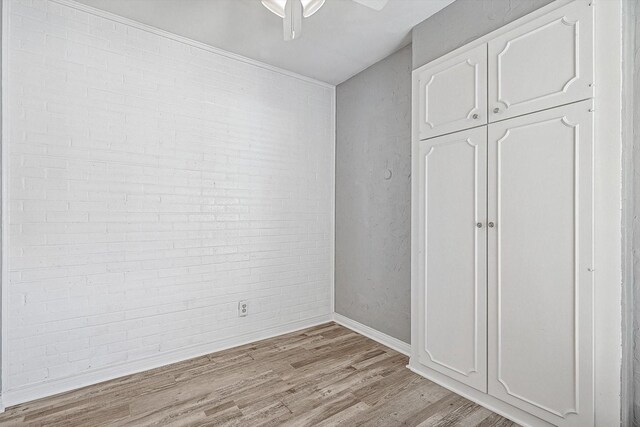 unfurnished bedroom featuring a closet, light wood-style floors, ceiling fan, brick wall, and baseboards