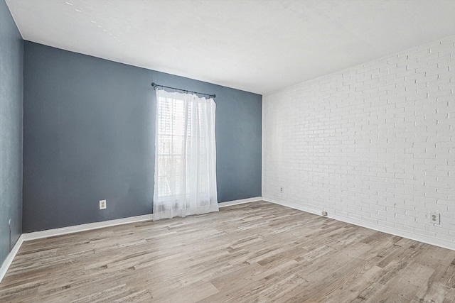 spare room featuring baseboards, brick wall, and wood finished floors