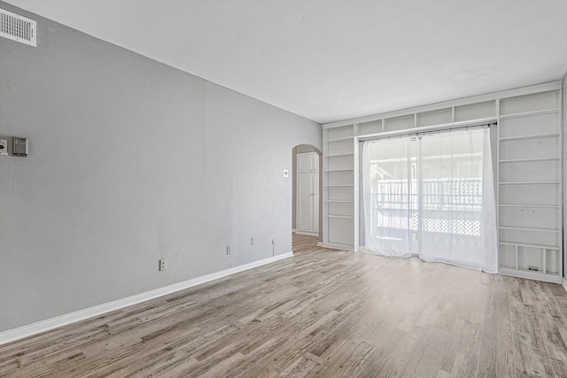 spare room featuring built in shelves, arched walkways, visible vents, wood finished floors, and baseboards