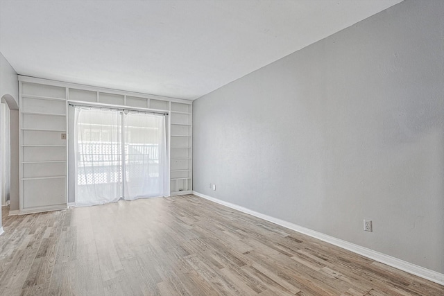 spare room featuring built in shelves, arched walkways, baseboards, and wood finished floors