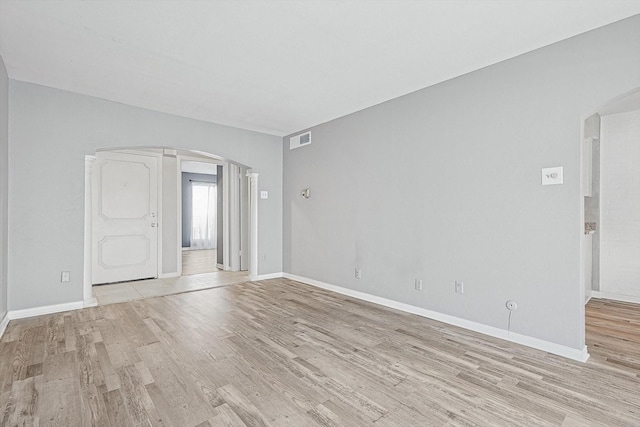 spare room featuring light wood-type flooring, arched walkways, visible vents, and baseboards