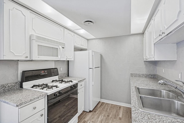 kitchen featuring light countertops, white cabinets, a sink, light wood-type flooring, and white appliances