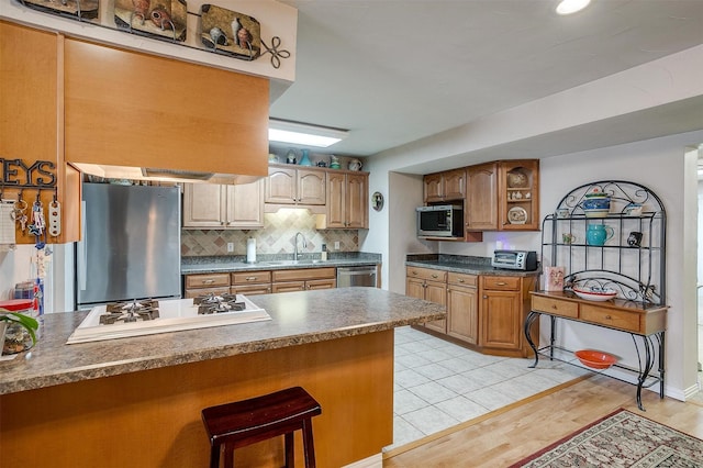 kitchen with a kitchen breakfast bar, stainless steel appliances, light wood-type flooring, decorative backsplash, and sink