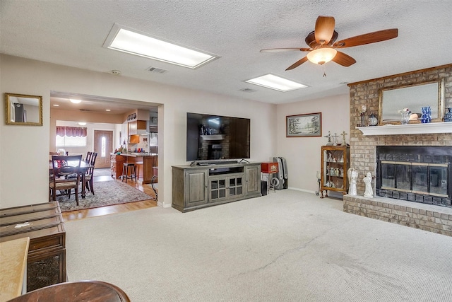 carpeted living room with a textured ceiling, ceiling fan, and a fireplace