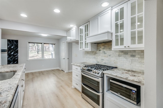 kitchen with light stone countertops, custom range hood, appliances with stainless steel finishes, tasteful backsplash, and white cabinetry