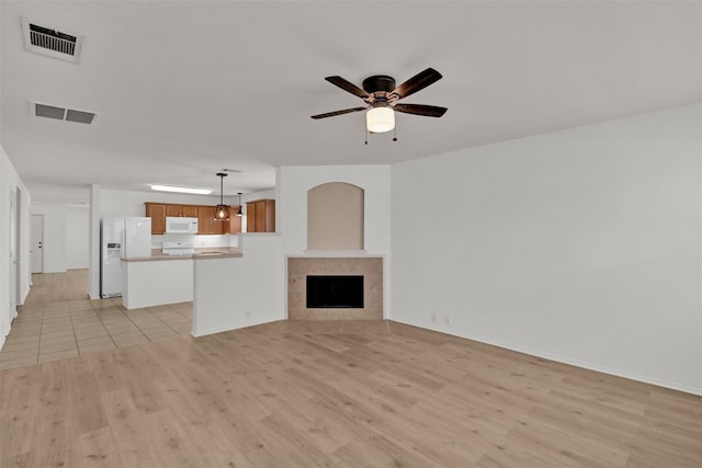 unfurnished living room with a tiled fireplace, ceiling fan, and light wood-type flooring