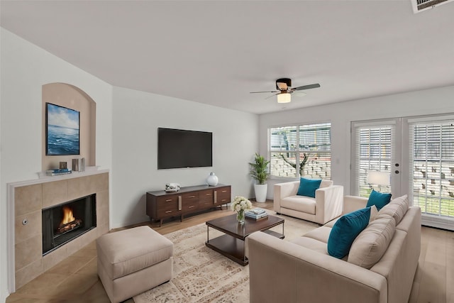 living room with a tile fireplace, ceiling fan, light hardwood / wood-style floors, and french doors