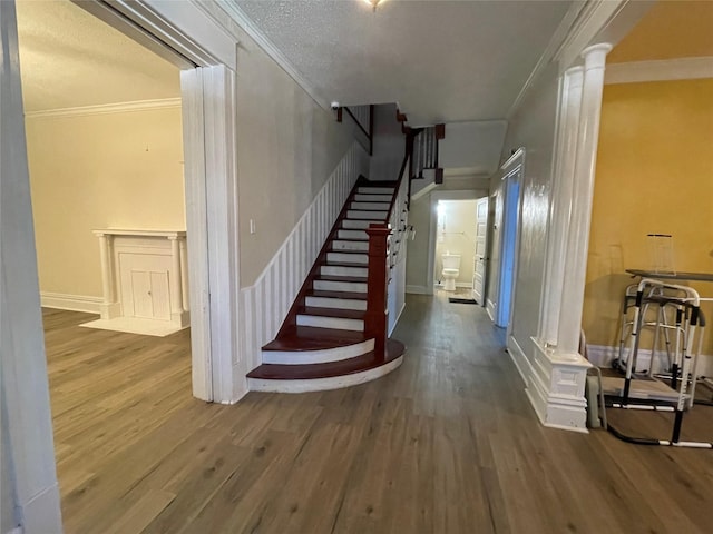 stairs featuring crown molding, decorative columns, and hardwood / wood-style floors