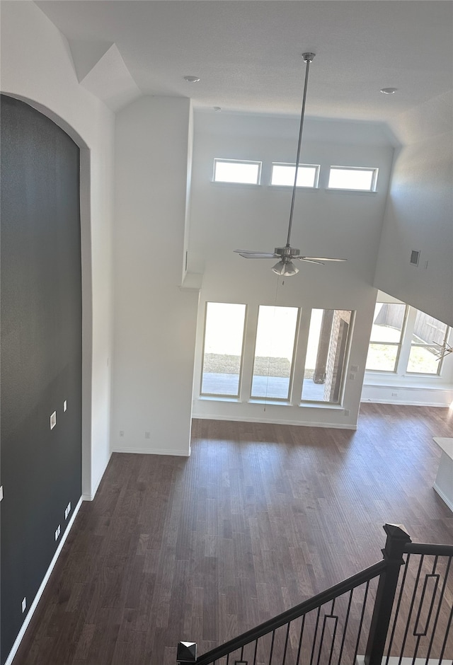 unfurnished living room featuring a towering ceiling, a wealth of natural light, dark wood-type flooring, and ceiling fan