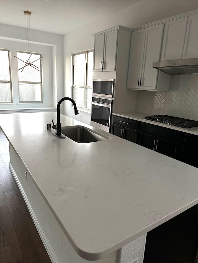 kitchen featuring pendant lighting, backsplash, sink, appliances with stainless steel finishes, and light stone counters