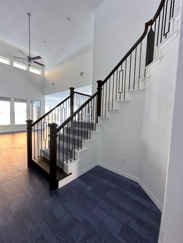 staircase with ceiling fan, wood-type flooring, and a high ceiling