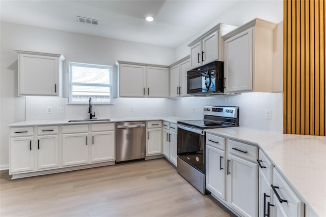 kitchen with sink, backsplash, stainless steel appliances, light stone counters, and light hardwood / wood-style floors