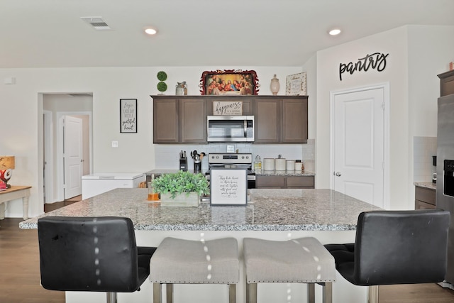 kitchen with stainless steel appliances, dark brown cabinetry, a kitchen island, and light stone countertops