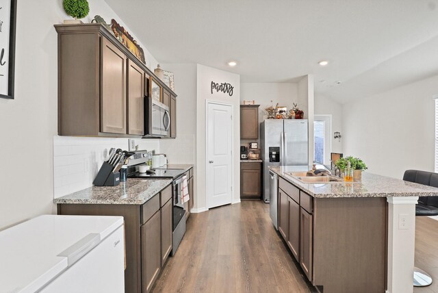 kitchen featuring a kitchen bar, wood-type flooring, stainless steel appliances, sink, and a kitchen island with sink