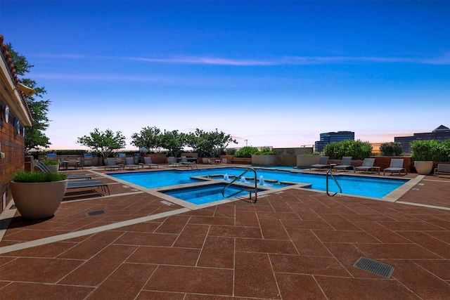 pool at dusk with a community hot tub and a patio