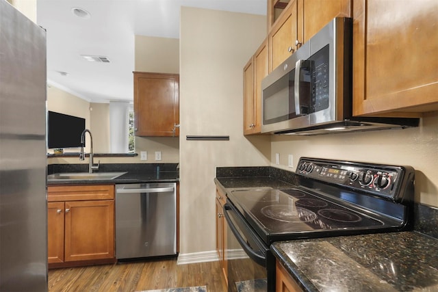 kitchen featuring stainless steel appliances, light hardwood / wood-style flooring, dark stone countertops, and sink