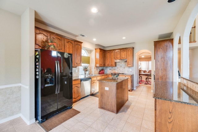 kitchen with black fridge, light tile patterned floors, dark stone countertops, dishwasher, and a kitchen island