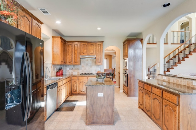 kitchen with a center island, sink, stainless steel appliances, light stone counters, and decorative backsplash