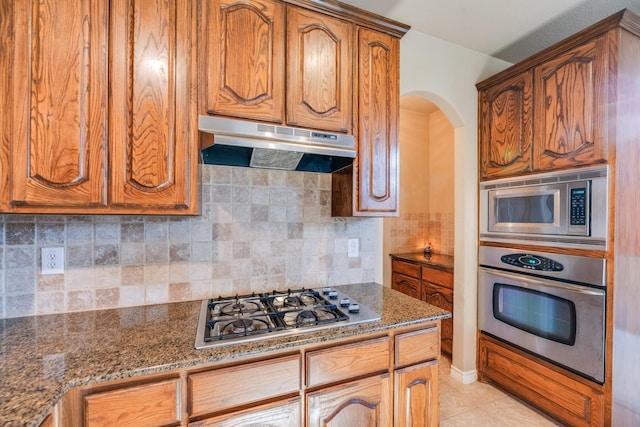 kitchen with decorative backsplash, light tile patterned floors, stainless steel appliances, and dark stone counters