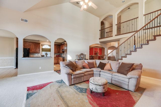 carpeted living room featuring ceiling fan and a towering ceiling