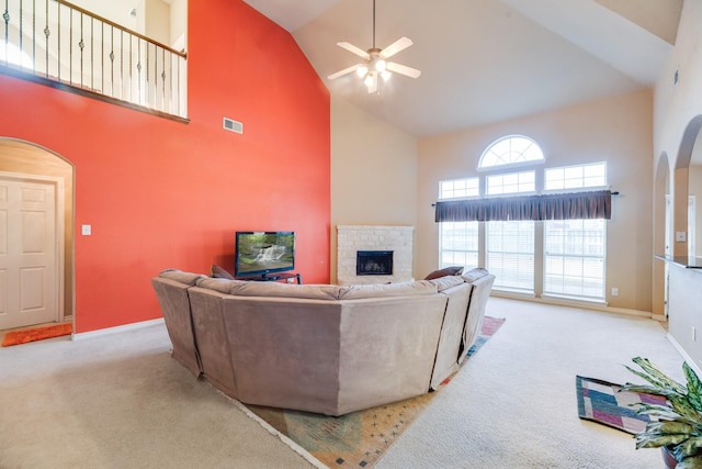 living room featuring a tile fireplace, light carpet, a towering ceiling, and ceiling fan